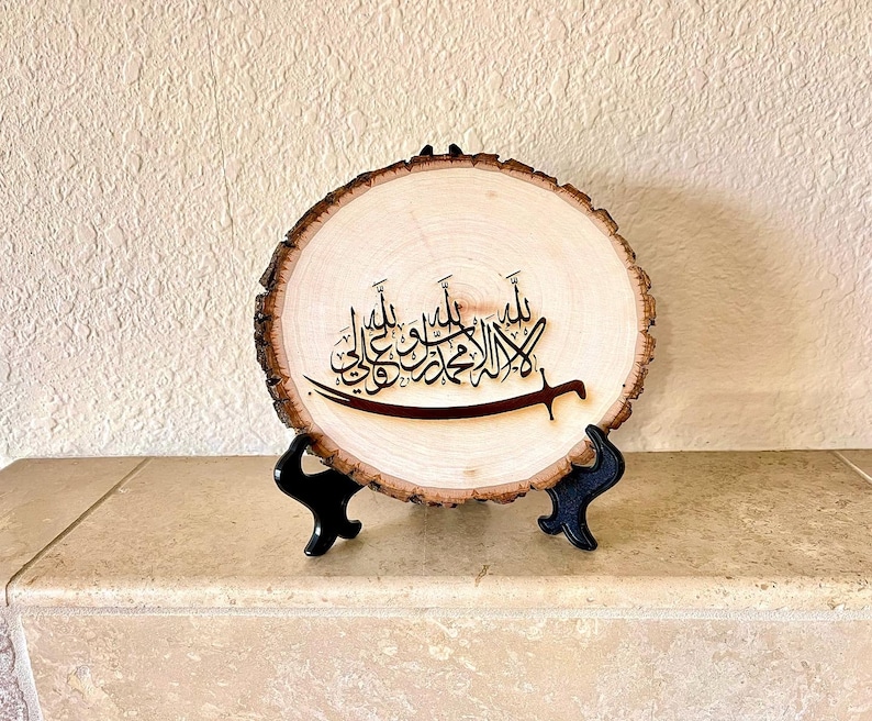 May include: A wooden round sign with a black Arabic calligraphy design on a natural wood background. The sign is on a black stand.
