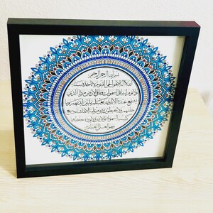 May include: A framed print with a blue and gold mandala design. The center of the mandala features a circular inscription in Arabic script. The inscription reads: "Bismillah ir-Rahman ir-Rahim, Allah hu al-ilah la ilaha illa hu al-haiy al-qayyum, la ta'khuzuhu sinatu wa la nawm, lahu ma fi al-samawati wa ma fi al-ard, man dhalika alladhi yashfa'u 'inda hu illa bi-idhn, ya'lamu ma baina aidihim wa ma khalfahum wa la yuhituna bi-shai min 'ilmihi illa bi-ma sha'a, wasi'a kursiyyuhu al-samawati wa al-ard, wa la ya'uduhu hifzuhuma wa hu al-'aliy al-'azim."