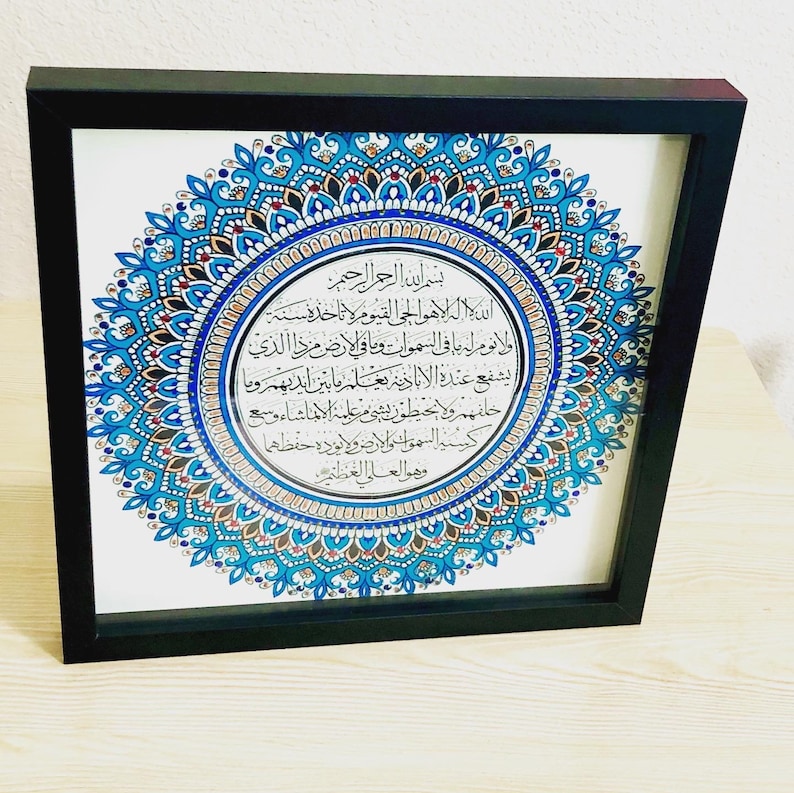 May include: A framed print with a blue and gold mandala design. The center of the mandala features a circular inscription in Arabic script. The inscription reads: "Bismillah ir-Rahman ir-Rahim, Allah hu al-ilah la ilaha illa hu al-haiy al-qayyum, la ta'khuzuhu sinatu wa la nawm, lahu ma fi al-samawati wa ma fi al-ard, man dhalika alladhi yashfa'u 'inda hu illa bi-idhn, ya'lamu ma baina aidihim wa ma khalfahum wa la yuhituna bi-shai min 'ilmihi illa bi-ma sha'a, wasi'a kursiyyuhu al-samawati wa al-ard, wa la ya'uduhu hifzuhuma wa hu al-'aliy al-'azim."