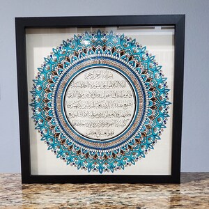 May include: A framed artwork featuring a blue and gold mandala with Arabic calligraphy in the center. The calligraphy reads "Bismillah ir-Rahman ir-Rahim" which translates to "In the name of Allah, the Most Gracious, the Most Merciful."