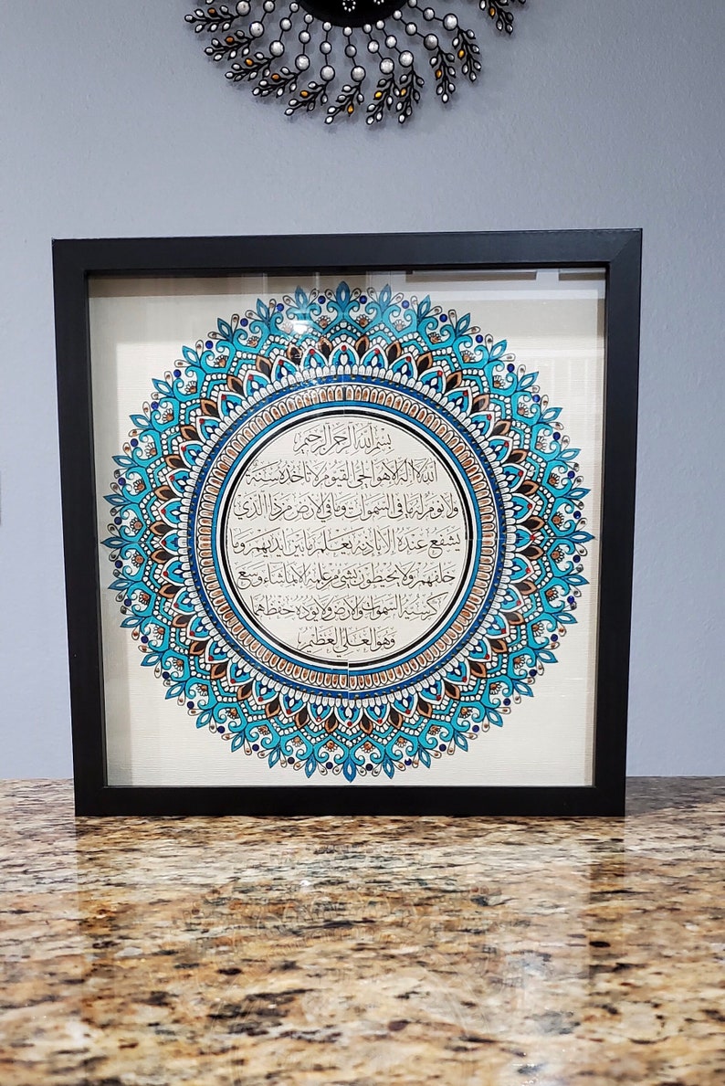 May include: A framed artwork featuring a blue and gold mandala with Arabic calligraphy in the center. The calligraphy reads "Bismillah ir-Rahman ir-Rahim" which translates to "In the name of Allah, the Most Gracious, the Most Merciful."