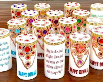 May include: A group of white candles decorated with colorful jewels and gold trim. The candles have a message that reads "May this Festival of Lights illuminate your home and lives with lots of love, joy and prosperity!" and "Happy Diwali".