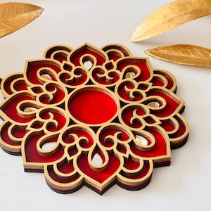 Pode incluir: Uma base para copos decorativa de madeira em camadas com um design floral. A base para copos apresenta um centro vermelho e detalhes intrincados em dourado. Folhas douradas estão no fundo. Esta base para copos é um item de decoração para casa único.