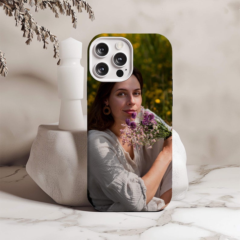 May include: A black phone case with a photo of a woman holding a bouquet of purple flowers. The phone case has a white camera bump with four lenses.