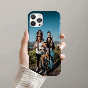May include: A blue phone case with a photo of a family of six. The family is standing in a field with green grass and blue sky. The phone case has a camera lens cutout.