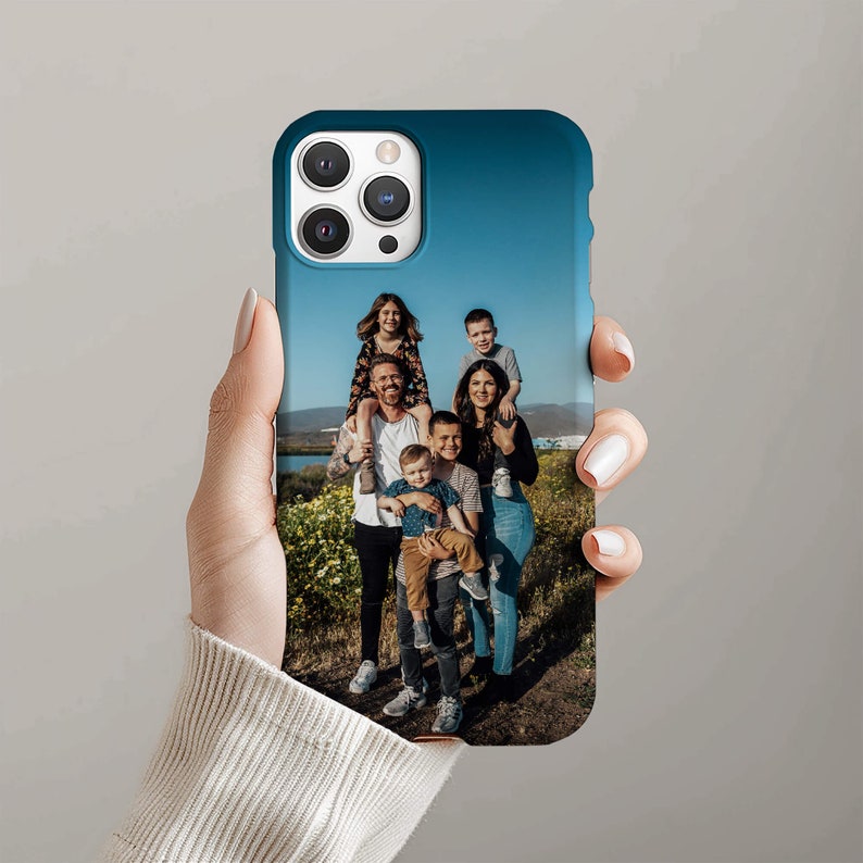 May include: A blue phone case with a photo of a family of six. The family is standing in a field with green grass and blue sky. The phone case has a camera lens cutout.