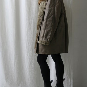 May include: A brown leather coat with a faux fur lining. The coat is worn by a person wearing black tights and black ankle boots.