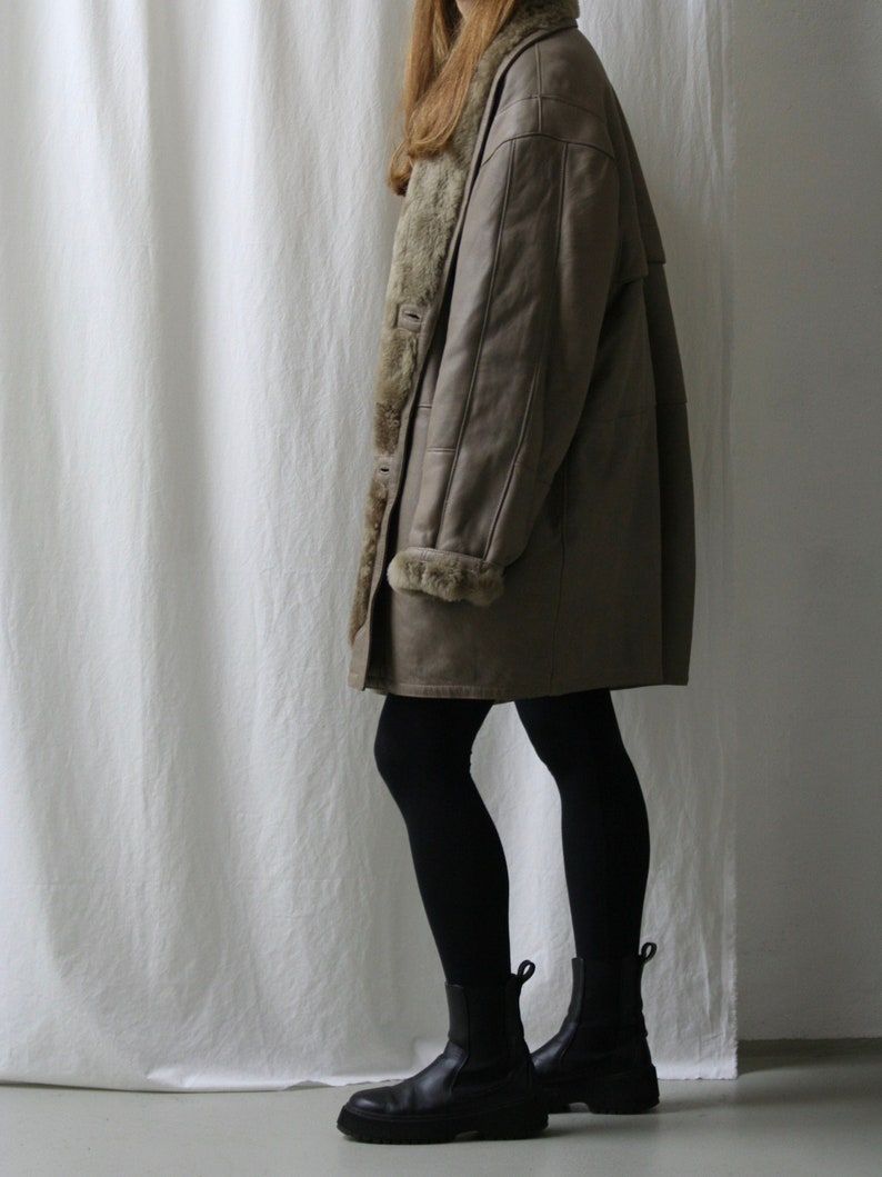 May include: A brown leather coat with a faux fur lining. The coat is worn by a person wearing black tights and black ankle boots.