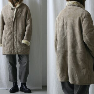 May include: A long, beige shearling coat with a fur collar and a zipper closure. The coat has a relaxed fit and is made of a soft, luxurious material.