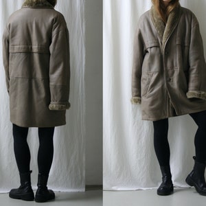 May include: A long brown leather coat with a fur collar and lining. The coat has a button closure and two pockets. The coat is being worn by a person with black leggings and black ankle boots.