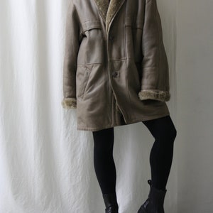 May include: A brown leather coat with a fur collar and lining. The coat has a single button closure and two pockets. The model is wearing black leggings and black ankle boots.