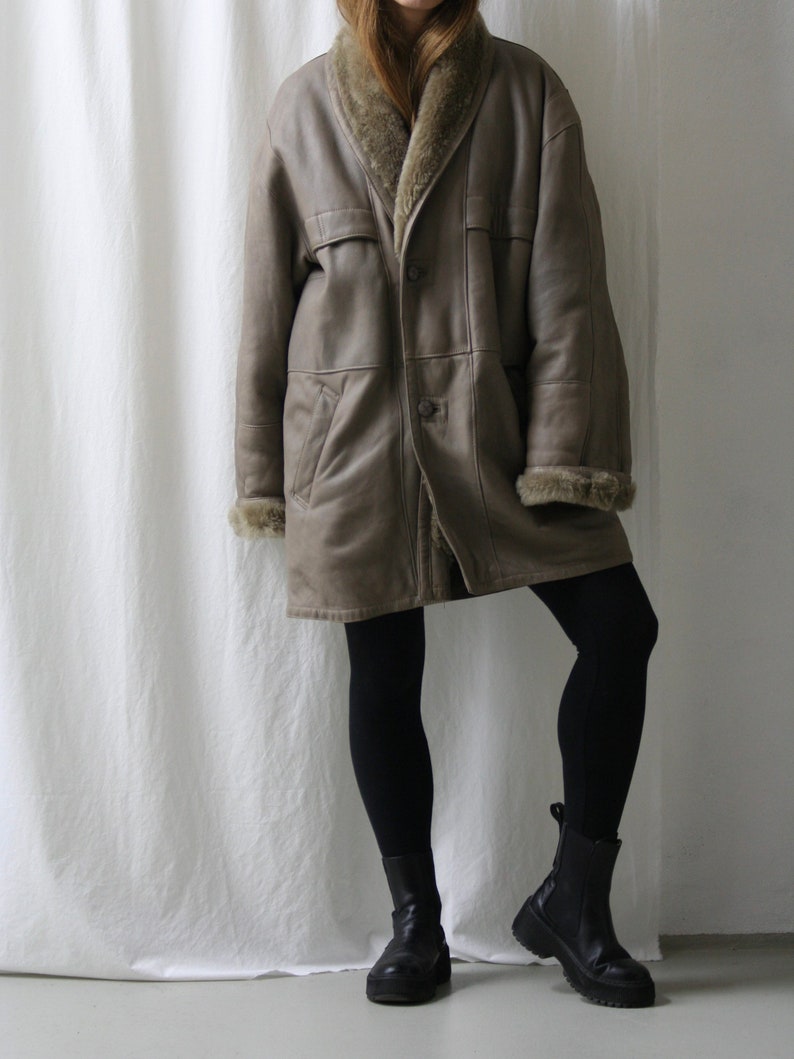 May include: A brown leather coat with a fur collar and lining. The coat has a single button closure and two pockets. The model is wearing black leggings and black ankle boots.