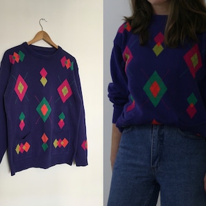 May include: Purple sweater with a diamond pattern in pink, green, yellow, and red. The sweater has two pockets.