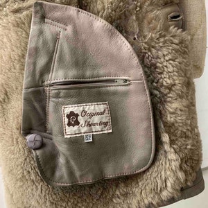 May include: A brown shearling jacket with a large patch pocket on the left side. The pocket has a zipper and a label that reads "Original Shearling 52".