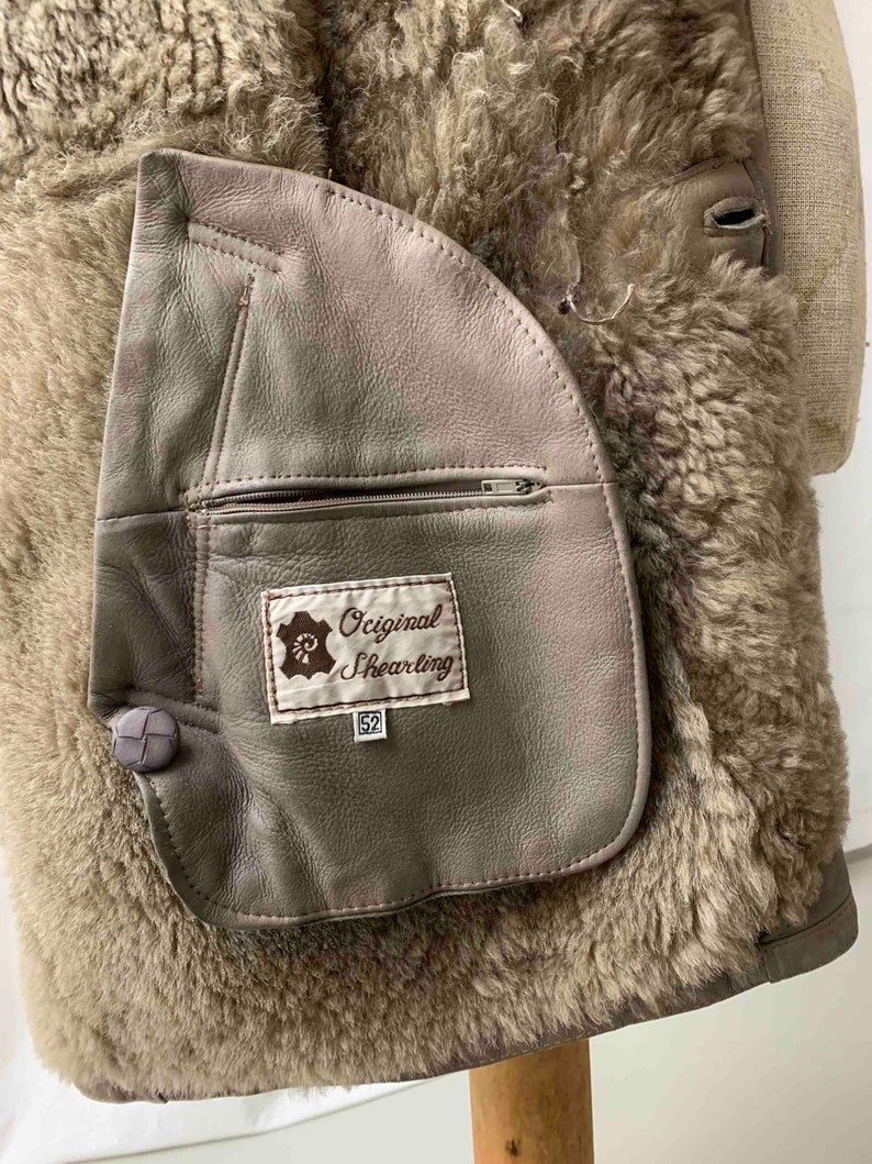 May include: A brown shearling jacket with a large patch pocket on the left side. The pocket has a zipper and a label that reads "Original Shearling 52".