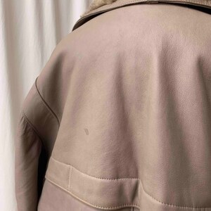 May include: A light brown leather jacket with a faux fur collar. The jacket has a zipper closure and a flap pocket on the front.