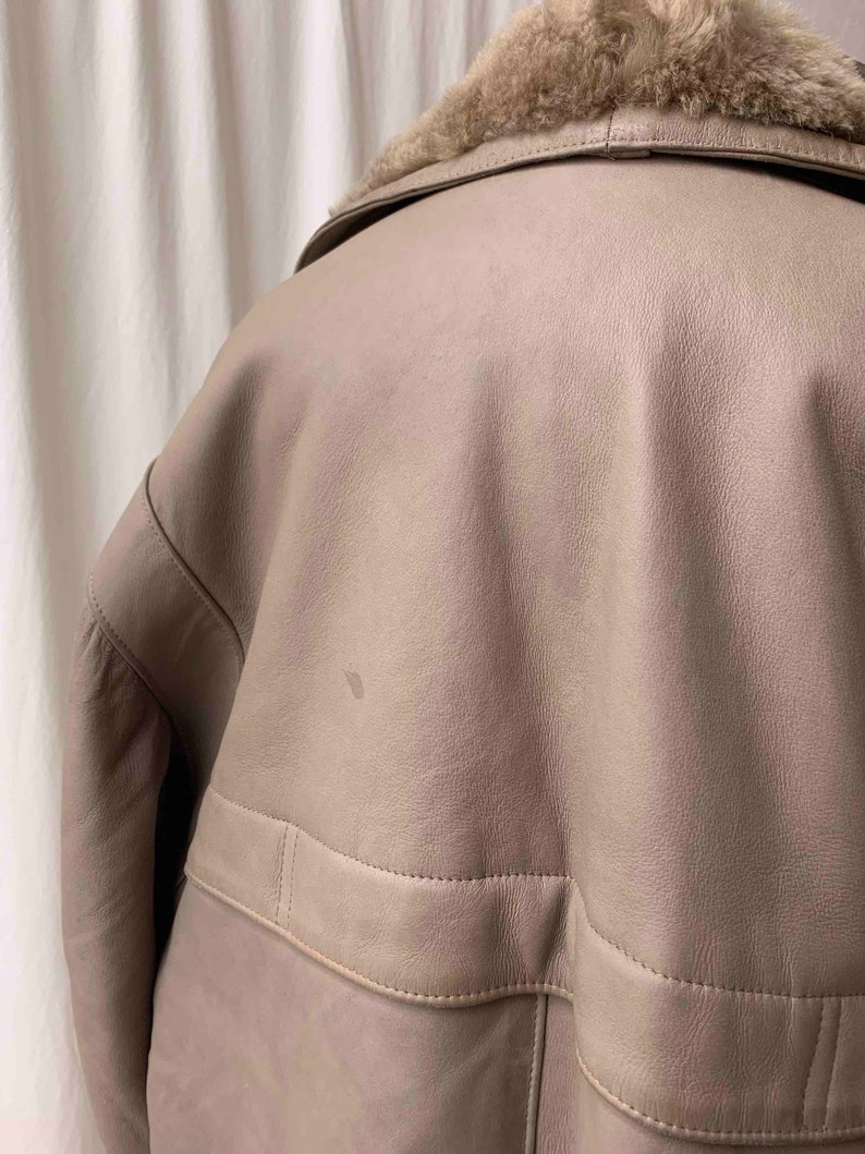 May include: A light brown leather jacket with a faux fur collar. The jacket has a zipper closure and a flap pocket on the front.