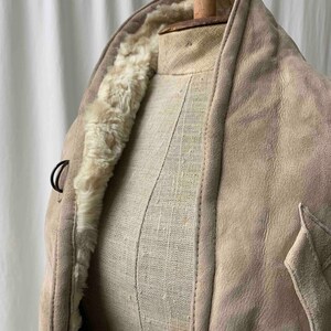 May include: A beige suede jacket with a faux fur lining. The jacket has a collar and a button closure.
