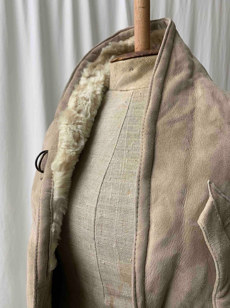 May include: A beige suede jacket with a faux fur lining. The jacket has a collar and a button closure.