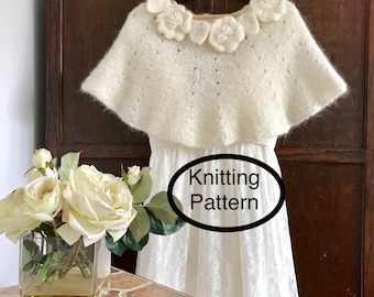 Może przedstawiać: Biały, dzianinowy szal z haftowanymi kwiatami. Szal wisi na drewnianym wieszaku na tle drewnianej ściany. Na zdjęciu widoczny jest napis "Knitting Pattern".