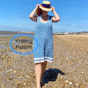 Op de afbeelding: Een lichtblauwe gebreide jurk met een witte bies en een V-hals ontwerp. De jurk heeft een uniek patroon en wordt gedragen met een strohoed met een kleurrijk lint. De tekst "Knitting Pattern" is zichtbaar.