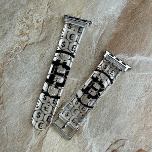 May include: Two clear watch bands with silver hardware. The bands feature a black and white honeycomb pattern with dollar, euro, and pound symbols. The bands are displayed on a textured, light brown surface.