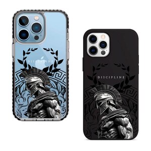 May include: Two phone cases with a black and white image of a Spartan warrior wearing a helmet and holding a spear. The image is surrounded by a laurel wreath and a Greek key pattern. The text "DISCIPLINE" is printed on the case.