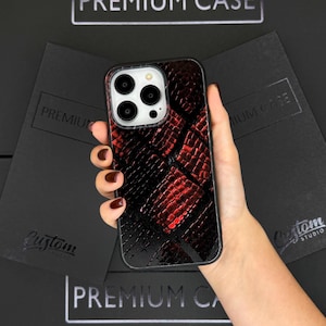 May include: Red and black snakeskin patterned phone case for an iPhone. The case has a raised camera bump and a black border.