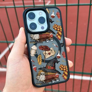 Puede incluir: Una funda de teléfono negra con fondo gris y un patrón colorido de ilustraciones con temática de Harry Potter. Las ilustraciones incluyen un libro, una pluma de ave, una carta, una jaula, un sombrero y una bufanda. La funda tiene una parte posterior transparente y un marco negro.