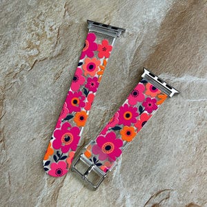 Pode incluir: Uma pulseira de relógio transparente com um padrão floral vibrante em tons de rosa, laranja e azul escuro. A pulseira inclui conectores de metal prateado e uma fivela prateada, concebidos para fixação a uma caixa de relógio digital.