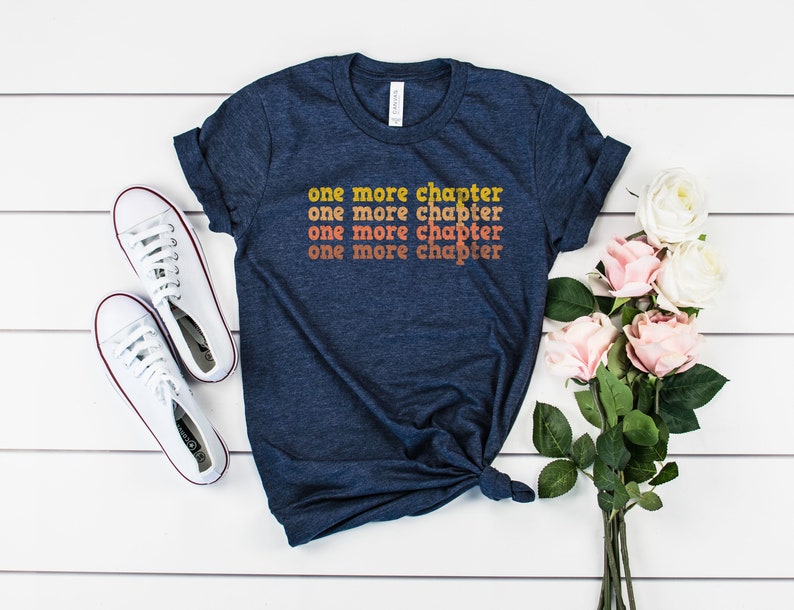May include: A navy blue t-shirt with the text "one more chapter" repeated four times in a gradient of orange, yellow, and white.
