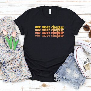 May include: Black t-shirt with the text "one more chapter" repeated four times in a retro font with orange and yellow colors.