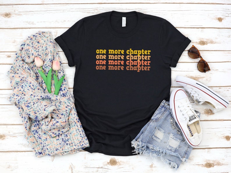 May include: Black t-shirt with the text "one more chapter" repeated four times in a retro font with orange and yellow colors.