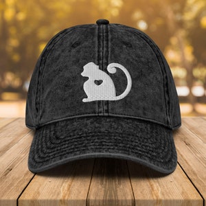 May include: A black denim baseball cap with a white embroidered image of a monkey with a heart on its chest.