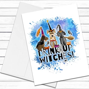 May include: A Halloween greeting card featuring three dogs dressed as witches, with the text "DRINK UP WITCHES!" in a blue watercolor splash. The dogs wear witch hats and hold bowls and a broom. The card is white with a matching envelope.
