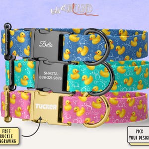 May include: Three pet collars featuring a yellow rubber duck and bubble pattern. The top collar is blue with a black buckle engraved with Bella. The middle is teal with a black buckle engraved with Shasta and 888-321-9876. The bottom is pink with a gold buckle engraved with Tucker.