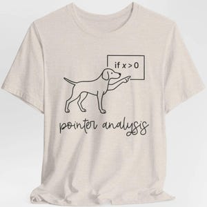 May include: Beige t-shirt featuring a black line drawing of a dog pointing at a sign that reads "if x > 0." Below the dog is the text "pointer analysis" in a handwritten style font. The shirt has short sleeves and a crew neck.