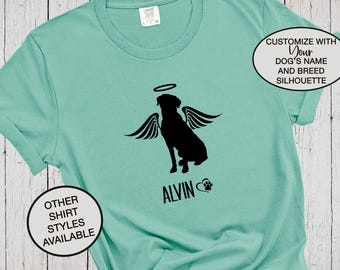 Puede incluir: Una camiseta verde menta con la silueta negra de un perro con alas de ángel y un halo. Debajo del perro, el nombre ALVIN está impreso junto a un pequeño icono de huella. Dos textos circulares dicen CUSTOMIZE WITH YOUR DOG'S NAME AND BREED SILHOUETTE y OTHER SHIRT STYLES AVAILABLE.
