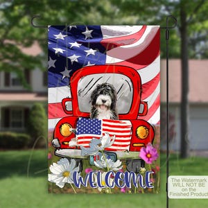 May include: A rectangular garden flag featuring a red vintage truck with a black and white dog in the driver seat. The background displays an American flag. The truck bed holds a smaller American flag. White and pink flowers sit below with the word WELCOME.
