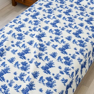 May include: White tablecloth with a blue toile pattern featuring gorillas, trees, and foliage. The fabric is draped over a table, showcasing the repeating design. The pattern is a classic, decorative style.