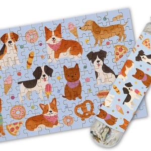 May include: A blue jigsaw puzzle with a variety of dogs wearing bandanas and enjoying treats like pretzels, donuts, and pizza. The puzzle pieces are in a tube with a silver lid.