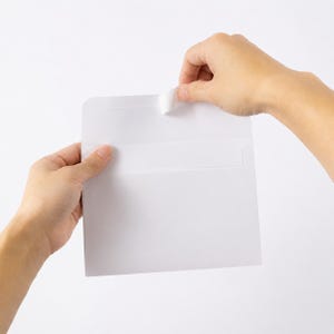 A person's hands are holding a blank white envelope against a plain white background.