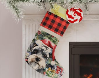 以下が含まれることがあります： 赤と黒のバッファローチェック柄の袖口が付いたクリスマスストッキング。サンタの帽子をかぶったシュナウザーのイラストがプリントされており、帽子の縁にはCOOPERという名前が記され、周囲にはカラフルなギフトボックスが描かれています。