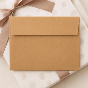 A brown envelope is placed on top of a white polka dot background, with a pink ribbon tied around it.