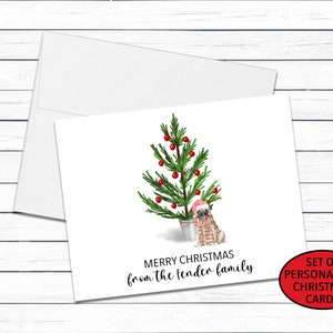 May include: A set of personalized Christmas cards featuring a watercolor illustration of a pug wearing a Santa hat and standing next to a small Christmas tree. The text on the card reads "Merry Christmas from the fender family".