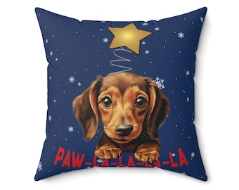May include: A blue throw pillow with a dachshund dog wearing a Christmas tree hat. The dog is looking at the camera and the text "PAW-LA-LA-LA-LA" is printed on the pillow.