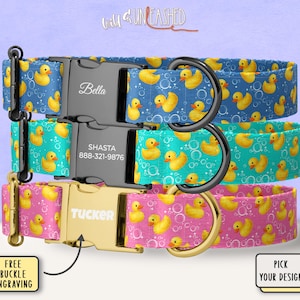 May include: Three personalized dog collars in blue, teal, and pink, each adorned with a pattern of yellow rubber ducks and bubbles. The collars feature engraved buckles with names and contact information.
