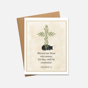 May include: A greeting card with a beige background and a gold border. The card features a cross made of green leaves, a black cat, and the text "Blessed are those who mourn, for they shall be comforted. MATTHEW 5:4."