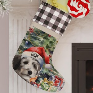 May include: A personalized Christmas stocking with a white dog wearing a Santa hat in front of a Christmas tree with presents. The stocking is decorated with a black and white buffalo plaid pattern. The dog's name is "Lusby".