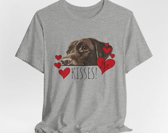 May include: A heather gray short-sleeve t-shirt featuring a graphic of a brown dog's head surrounded by red hearts. The text reads Kisses! and 25 cents, with the dog positioned above the text. The design is centered on the front of the shirt.